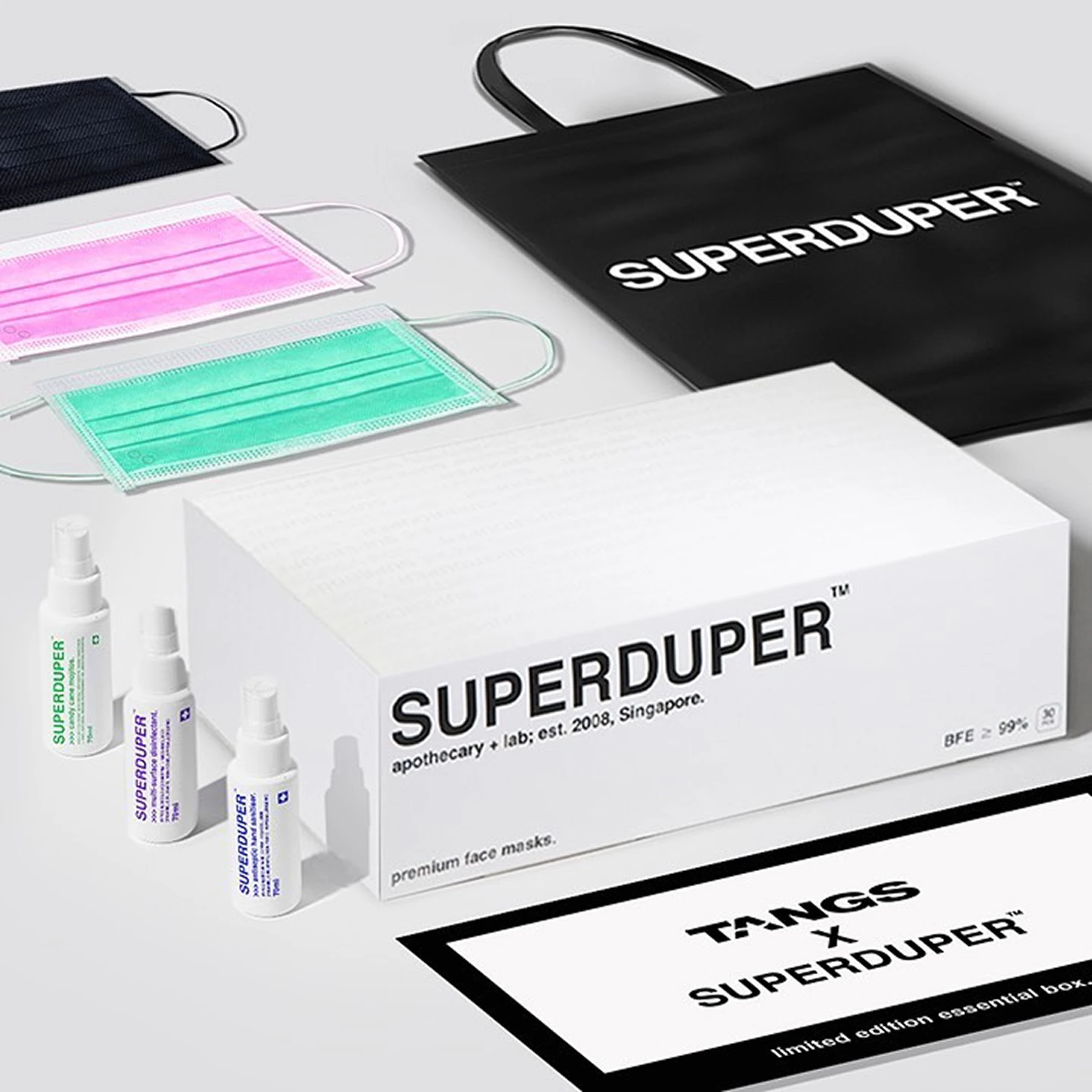 SUPERDUPER face masks, small spray bottles, a white product box and a black branded tote bag arranged on a pale studio surface.